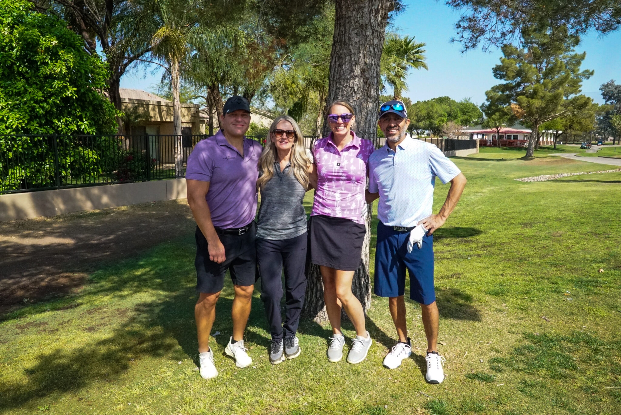 Team of four golfers smiling together under the trees
